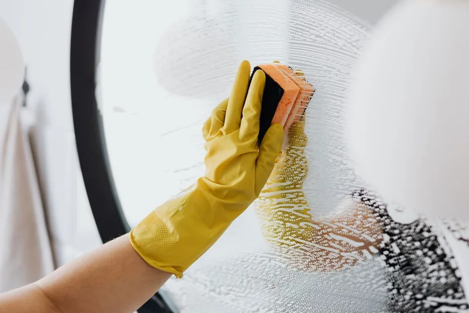 Een gehandschoende hand reinigt een spiegel met een spons